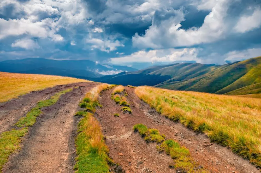 Zandpad door heuvelachtig landschap met bergen en wolkenlucht in Nieuw-Zeeland
